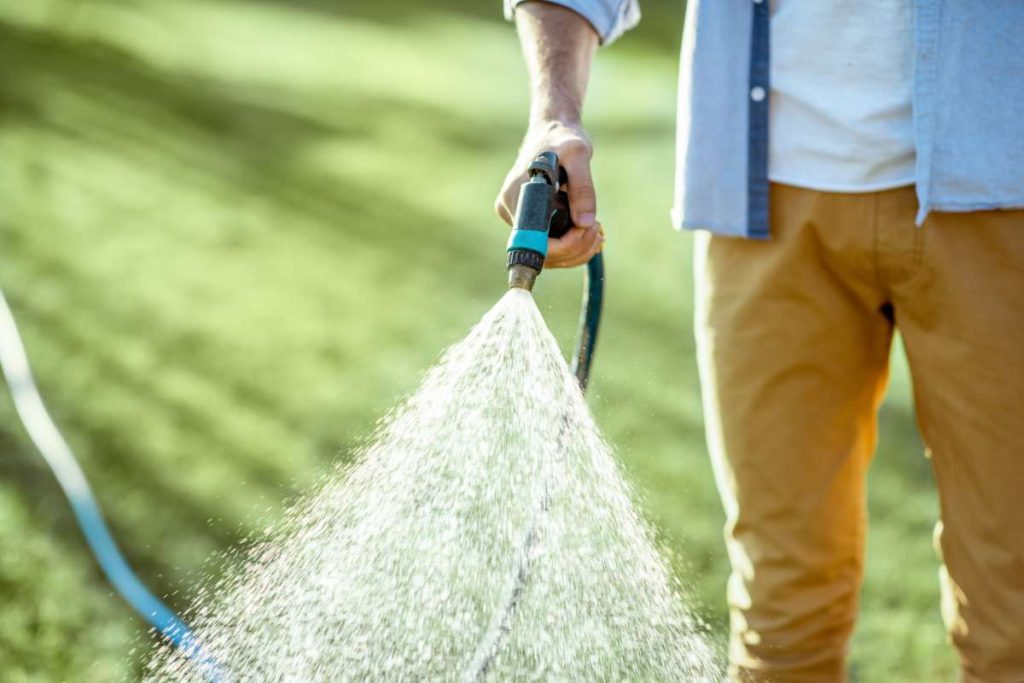 Man watering green lawn, sprinkling water on the grass with water pistol, close-up with no face